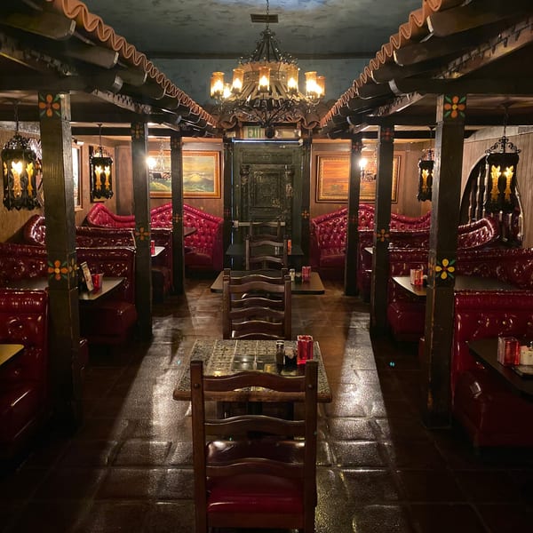 Ornate restaurant interior featuring red tufted booths, dark wood, tiled floors, and decorative lighting.