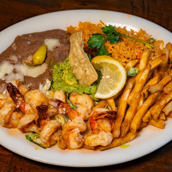 Plate of grilled shrimp, french fries, rice, refried beans, guacamole, and a lemon slice.