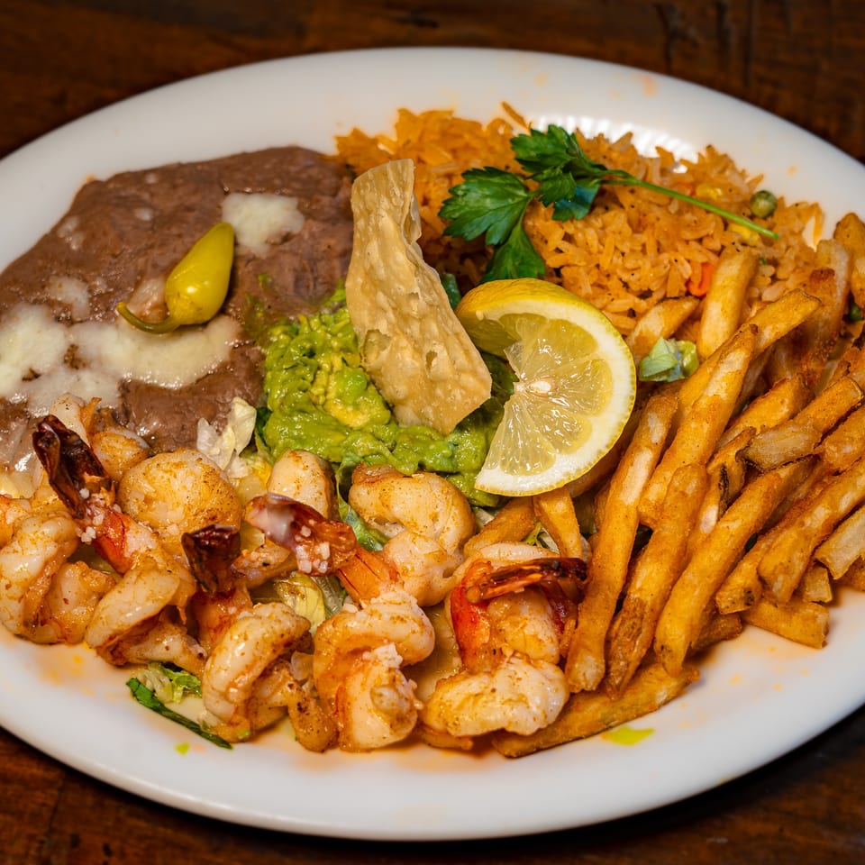 A plate of shrimp, refried beans, rice, guacamole, fries, and a lemon slice.
