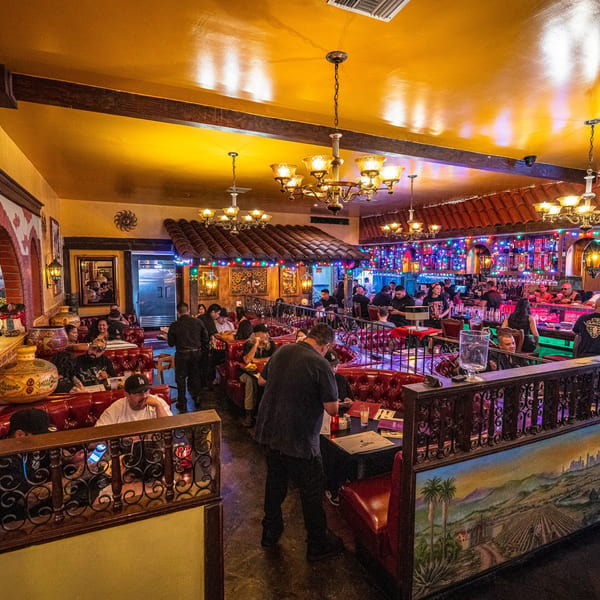 Lively restaurant interior with people dining in red booths and at a colorful bar.