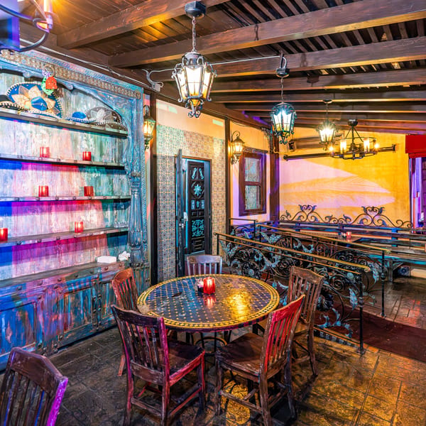 Colorful, ornately decorated restaurant interior with a round table, chairs, and illuminated shelves.