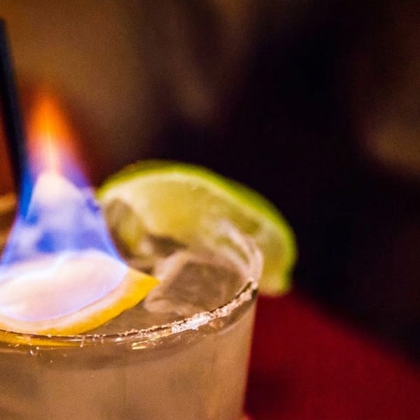 A flaming cocktail with a lemon slice and lime wedge, served in a salt-rimmed glass.