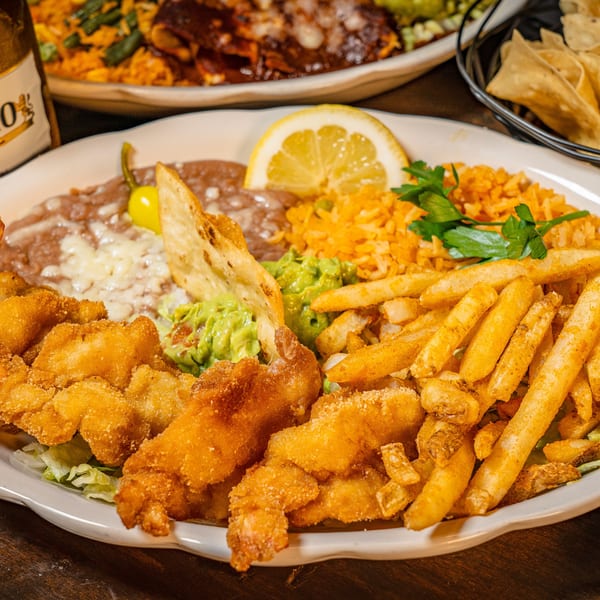 Fried shrimp and french fries with refried beans, rice, guacamole, and a lemon slice.