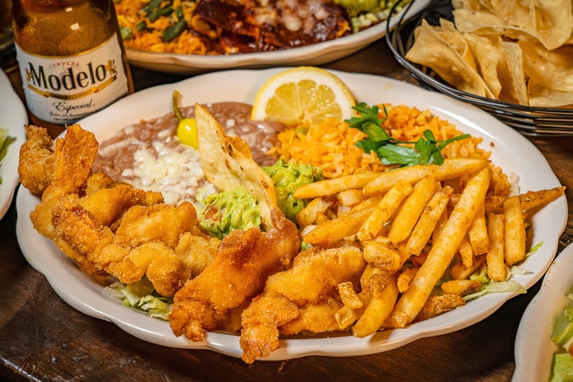 Fried shrimp and french fries with refried beans, rice, guacamole, and a lemon slice.