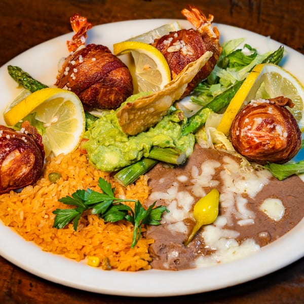 Plate of bacon-wrapped shrimp, rice, refried beans, guacamole, asparagus, and lemon slices.