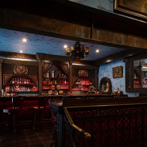Opulent bar interior featuring red tufted seating, glowing liquor bottles, and a decorative blue ceiling.