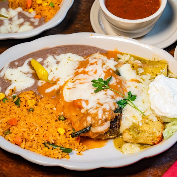Mexican combo plate featuring rice, refried beans, enchiladas, chile relleno, melted cheese, and sour cream.