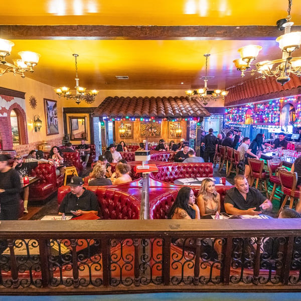 Lively Mexican restaurant interior with patrons dining in red booths and a vibrant bar.