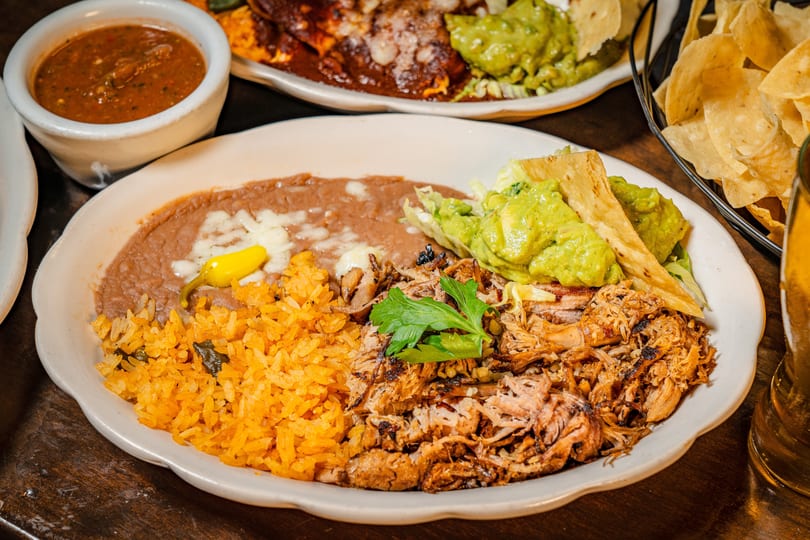 A plate of Mexican food with shredded pork, rice, refried beans, guacamole, and a side of salsa.