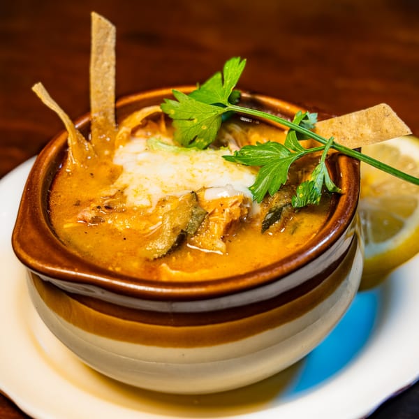 Hearty soup with melted cheese, parsley, tortilla strips, and a lemon wedge in a striped bowl.