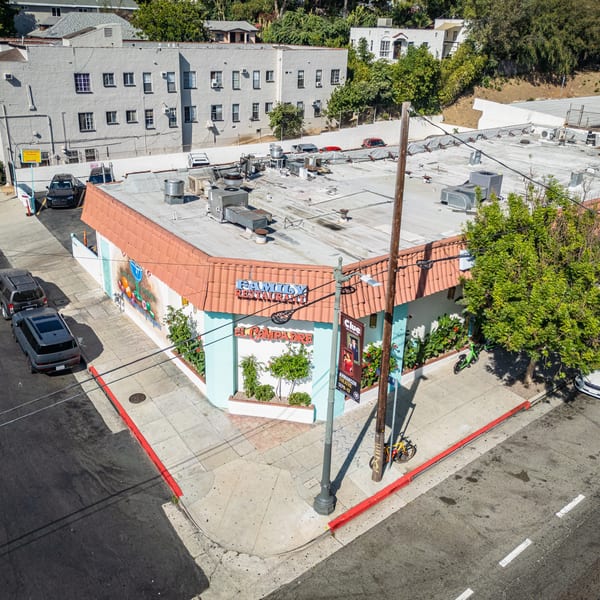 Aerial view of El Compadre Family Restaurant, a corner building with a red tile roof and vibrant murals.