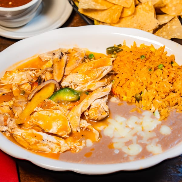 Mexican chicken stew with rice, cheesy refried beans, and tortilla chips on a table.