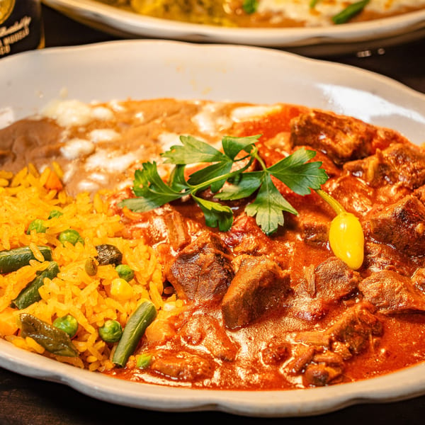 Hearty Mexican dish with stewed meat in red sauce, rice, refried beans, and a beer bottle.