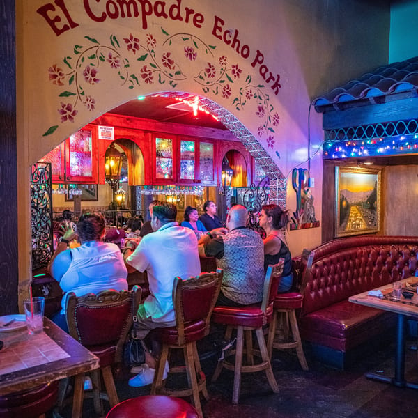 Patrons enjoy the vibrant, colorful interior of El Compadre Echo Park restaurant, featuring an arched entryway and bar seating.
