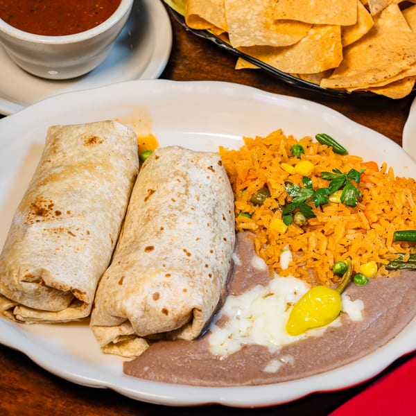 Plate with two burritos, Mexican rice, refried beans, and a yellow pepper, with chips and salsa.