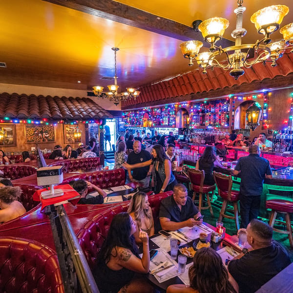 Lively restaurant interior with people dining in red booths and socializing at a colorful bar.