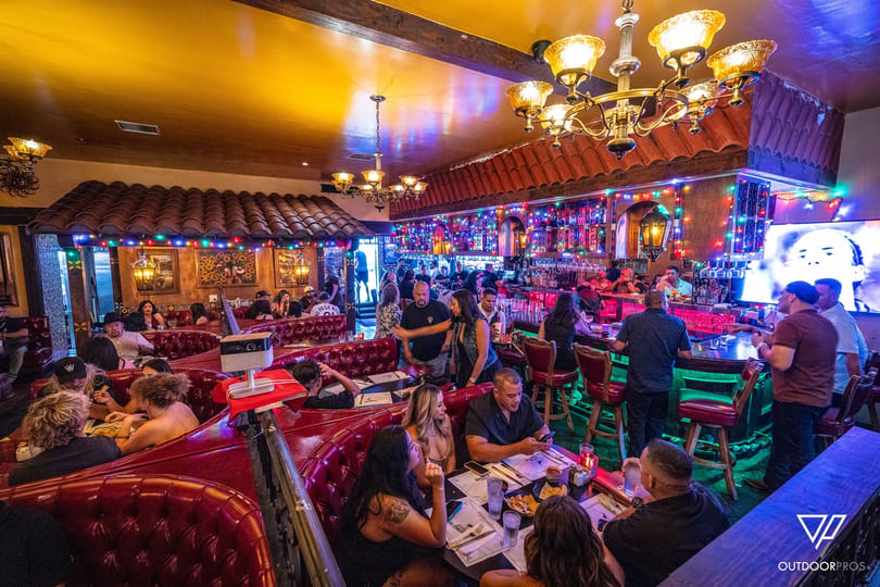 Lively restaurant interior with people dining in red booths and socializing at a colorful bar.