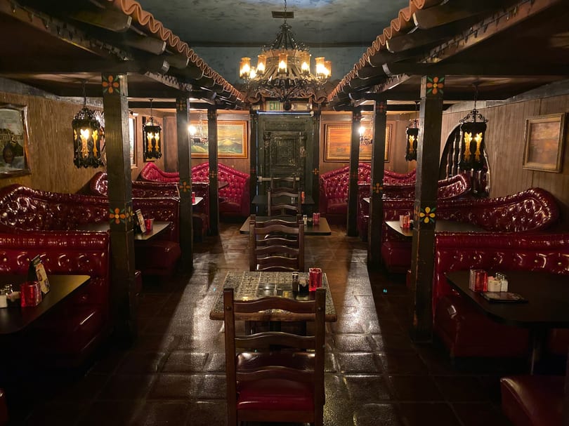 Dark, ornate dining room with red booths, wooden tables, and chandeliers, creating a cozy ambiance.