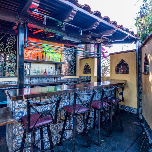 Outdoor bar with blue patterned tiles, bar stools, and liquor bottles on shelves.