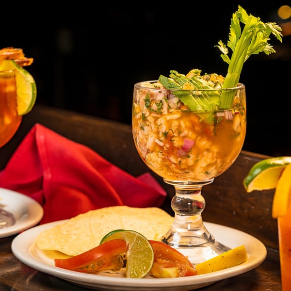 Two shrimp cocktails and a michelada on a dark table with a red napkin.