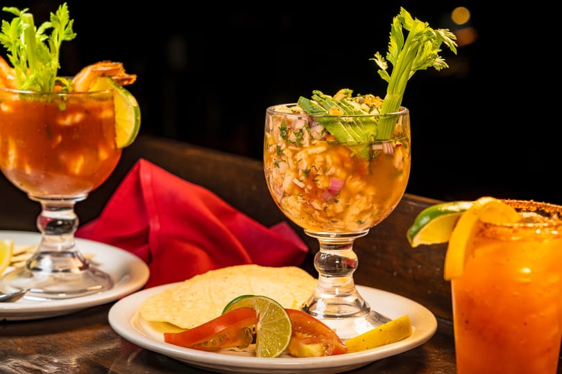 Two shrimp cocktails and a michelada on a dark table with a red napkin.