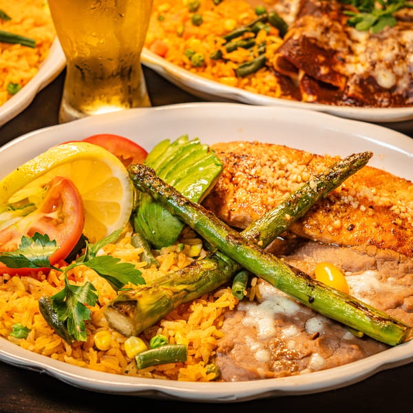 Grilled salmon with asparagus, rice, refried beans, avocado, and lemon on a white plate.