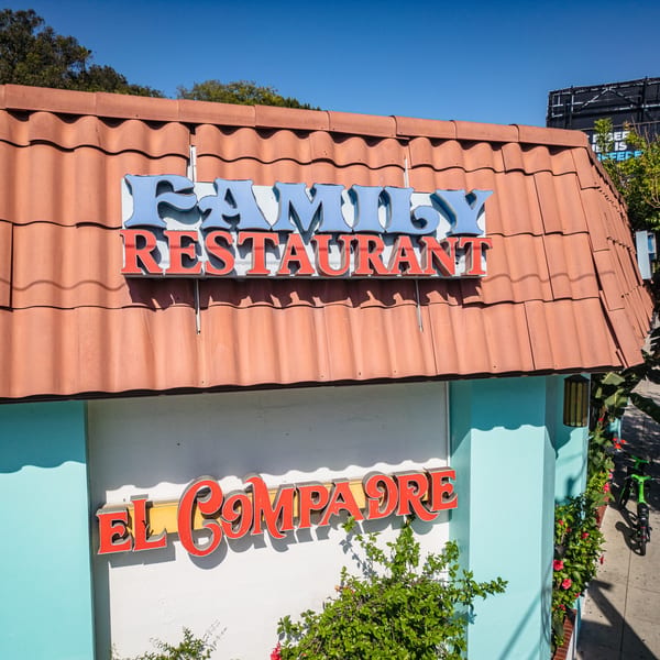 El Compadre Family Restaurant exterior with red tile roof, blue and red signs, and light blue walls.