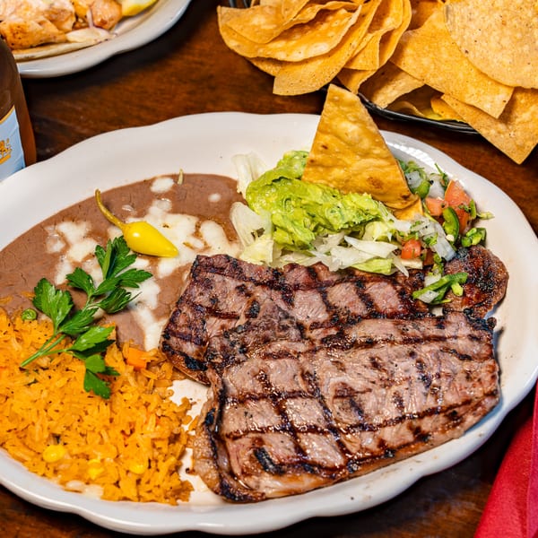 Grilled steak platter with rice, refried beans, salad, Modelo beer, chips, and salsa.
