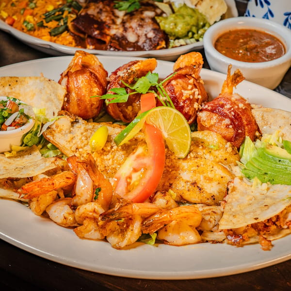 A large platter of grilled shrimp, bacon-wrapped shrimp, quesadillas, and fresh garnishes.