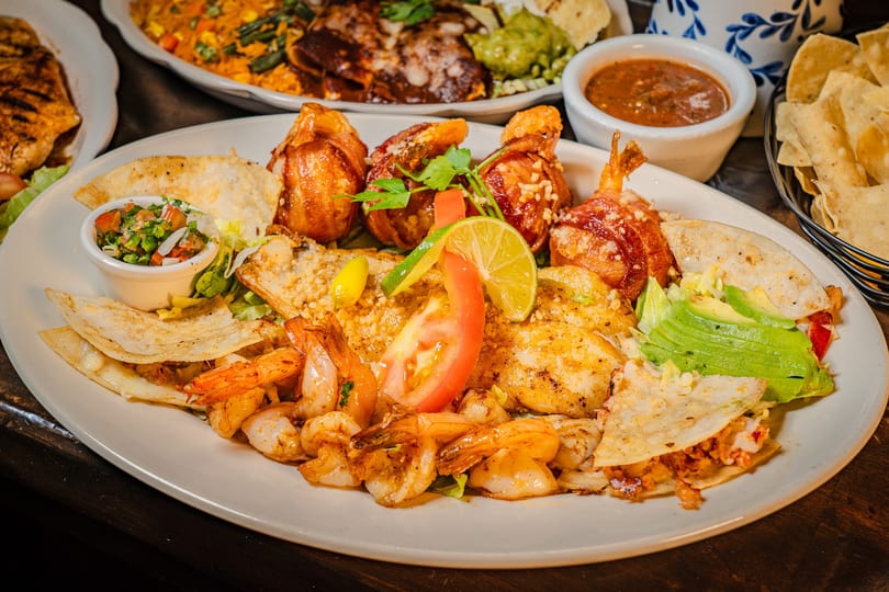 A large platter of grilled shrimp, bacon-wrapped shrimp, quesadillas, and fresh garnishes.